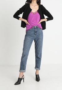 Svart ruggad jacka, lila satin camisole med spetsdetaljer, ljusblå jeans med uppvikta ärmar, svarta klackmules, minimalistisk design, avslappnad outfit.