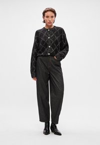 Cardigã preto cintilante com decote redondo e botões frontais, combinado com calças soltas cinza-escuras e botas de tornozelo pretas. Textura suave e ajuste relaxado.