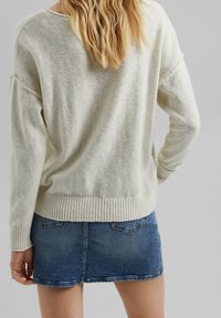 Jasno beżowy sweter z prążkowanym dołem i mankietami, w zestawieniu z krótką niebieską spódnicą dżinsową z tylnymi kieszeniami i postrzępionym dołem.