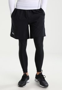 Black athletic shorts over black compression leggings, lightweight material, elastic waistband, with reflective logo accents and side pockets.