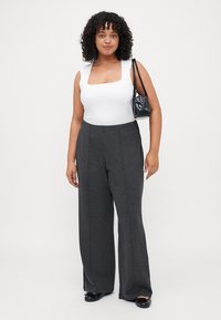 White square-neck sleeveless top paired with gray wide-leg pants. Model holds a small black textured handbag, wearing black slip-on shoes.