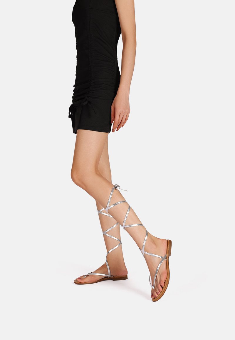 Sandali gladiator argento con lacci e suole piatte, caratterizzati da cinghie incrociate, punte aperte e un design minimalista.