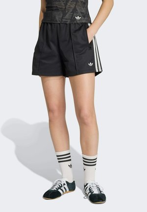 Sorte træningsshorts med hvide sidelister, med forlommer og elastisk taljebånd. Kombineret med hvide sokker med striber og grønne sko.