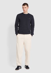 Granatowy sweatshirt z okrągłym dekoltem i ribbowymi mankietami, w połączeniu z jasnobeżowymi spodniami i czarnymi butami w białe paski. Prosty design.