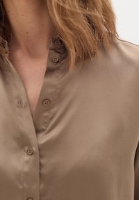 Brown silky blouse featuring a buttoned placket and a soft sheen, with a relaxed fit and a subtle collar design.