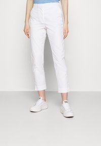 Vita cropped byxor i mjukt bomullsmaterial, med flat front, sidofickor och uppvikta fållar, i kombination med vita sneakers.