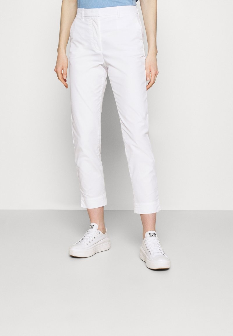 Vita cropped byxor i mjukt bomullsmaterial, med flat front, sidofickor och uppvikta fållar, i kombination med vita sneakers.