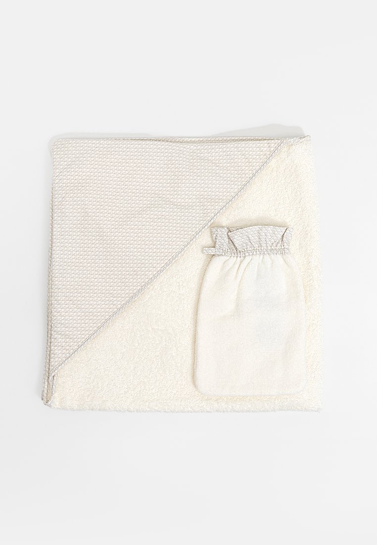 Toalla de algodón en color beige claro, con un patrón texturizado en una esquina y un pequeño bolsillo de malla adjunto. Material suave y absorbente.