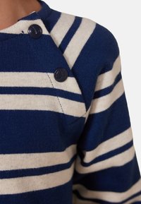 Marineblauer und creme gestreifter Pullover mit seitlichem Knopfverschluss. Strickstruktur; zwei Knöpfe an der Schulter für ein einfaches Anziehen.
