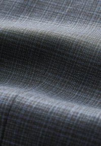 Tissu avec un motif écossais subtil dans des tons de vert foncé et de bleu. Texture lisse avec un léger éclat, mettant en valeur des détails de tissage complexes.