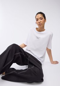 T-shirt bianco a maniche corte con testo ricamato, abbinato a pantaloni neri a gamba larga con dettagli di cucitura bianca. Tessuto testurizzato.