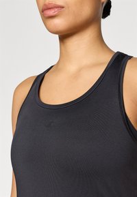 Μαύρο αθλητικό τοπ από λείο ύφασμα. Διαθέτει στρογγυλεμένο λαιμόκομμα, φαρδιές τιράντες και λεπτό λογότυπο στο κέντρο μπροστά.