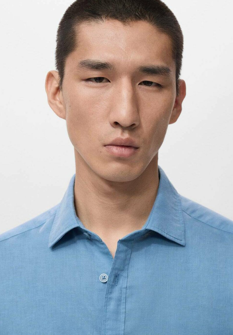 Hellblaues Hemd aus Baumwolle mit klassischem Kragen und feiner Textur. Vorderseite mit sichtbarer Zwei-Knopf-Leiste.