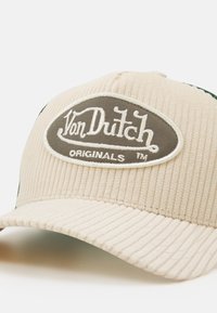 Casquette en velours côtelé beige avec un accent vert, ornée d'un patch ovale gris avec un texte brodé en blanc "Von Dutch ORIGINALS". Surface texturée.