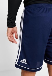 Shorts de sport bleu marine avec un design à trois bandes blanches et le logo Adidas sur l'ourlet gauche. Fabriqués en tissu lisse et léger.