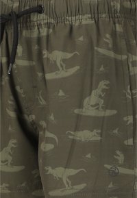 Olivgrüne Badekurze mit einem Dinosaurier- und Surfbrett-Muster, mit schwarzem Kordelzug, strukturiertem Material und seitlichen Taschen.