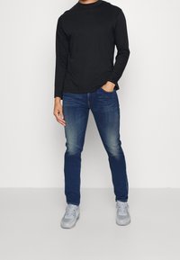 Svart långärmad tröja, denimblå jeans och grå sneakers. Avslappnad passform med rund halsringning och blekt denimtextur.