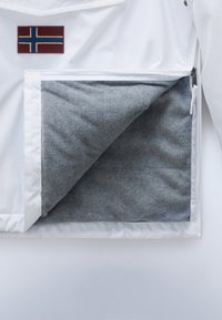 Weiße Jacke mit teilweise geöffnetem Frontfach, das ein weiches graues Fleecefutter und einen kleinen norwegischen Flaggen-Patch über dem Fach zeigt.