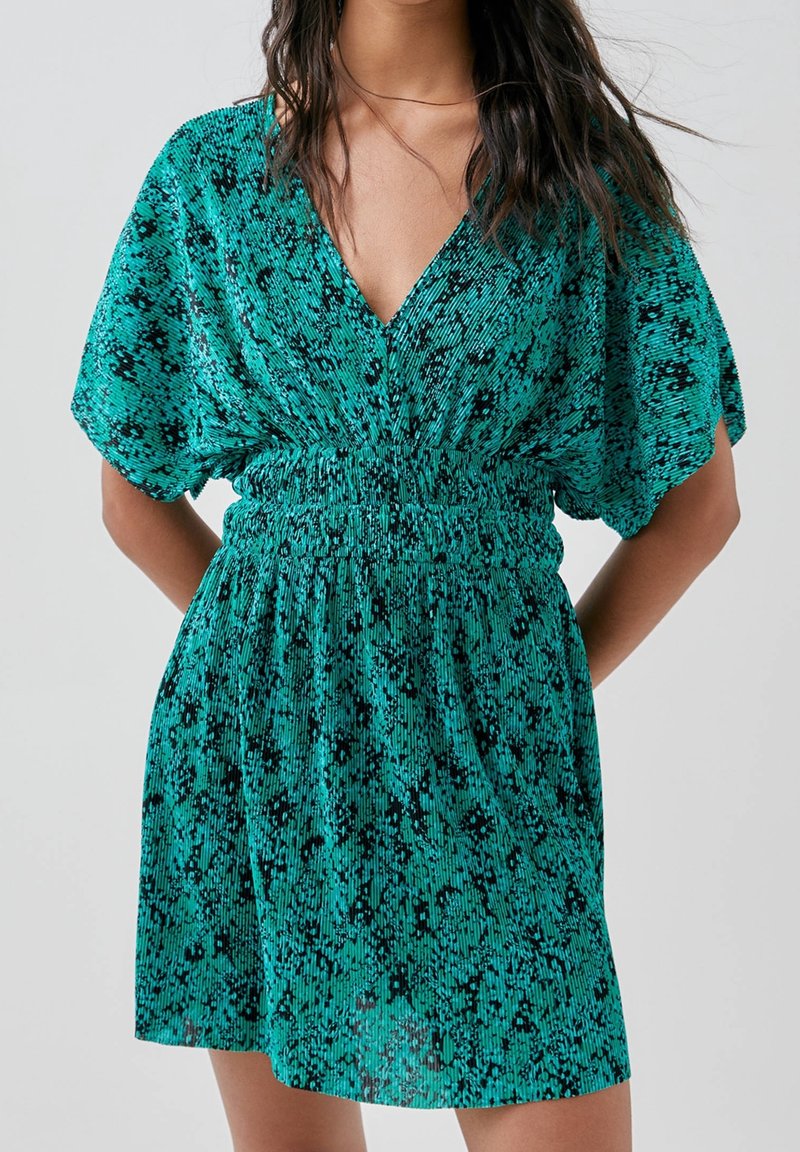 Robe courte teal avec un décolleté en V, manches dolman courtes, taille froncée et un motif texturé noir sur l'ensemble.