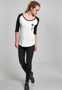 Witte en zwarte raglan T-shirt met een ronde halslijn, voorzien van een zwart bloemenafbeelding aan de linkerkant. Gecombineerd met zwarte skinny jeans.