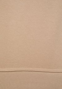 Béžová pletená tkanina s hladkým povrchem, se žebrovaným lemem. Design je jednoduchý a jednotný na celé ploše.