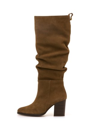 Botte en suède brun olive, montante jusqu'au genou, avec une tige flatteuse, un bout arrondi et un talon en bois empilé. Présente une languette pour un enfilage facile.