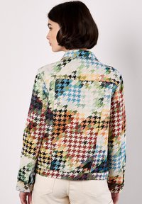 Chaqueta de mezclilla con estampado de pata de gallo multicolor, con cuello y mangas largas. Presenta tonos contrastantes de verde, azul y naranja.