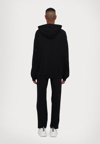 Felpa nera con cappuccio e pantaloni coordinati, realizzati in un tessuto morbido. Presenta una vestibilità comoda e maniche lunghe. Sneakers bianche con accenti neri.