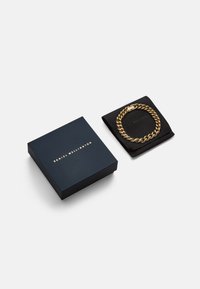 Auksinė grandinėlė ant juodo audinio maišelio, šalia tamsiai mėlynos dėžutės su auksinėmis raidėmis, pažymėta "DANIEL WELLINGTON."