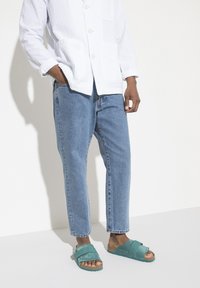 Hvid tekstureret skjorte med knapper, lys bl�å denimjeans og teal sandaler med blødt, polstret rem og åben tå.