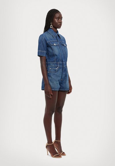 Salopetă din denim de culoare albastră închisă, cu mânecă scurtă, guler, fermoar frontal și două buzunare la piept. Accentuata cu o curea și pantaloni scurți conici.