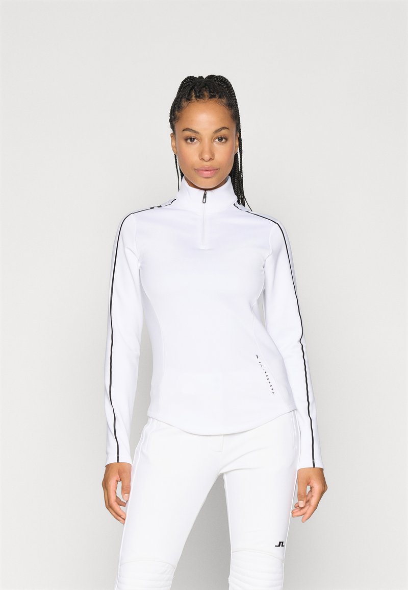 Top atletico bianco con zip al collo e maniche lunghe, caratterizzato da strisce laterali nere e una finitura texture lungo l'orlo e l'area della zip.