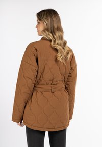 Bruine gewatteerde jas met een ceintuur in de taille, voorzien van een gestructureerd patroon en een relaxte pasvorm. Lange mouwen en een klassieke kraag maken het ontwerp compleet.
