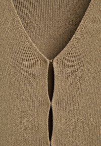 Beige knitted cardigan with a deep V-neck, featuring a front opening held together by a small metal clasp at the neck.