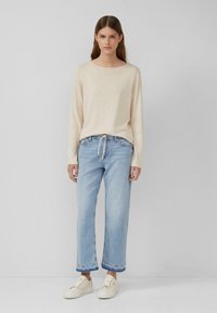 Maglietta a maniche lunghe beige chiaro con colletto rotondo, abbinata a jeans blu chiaro a gamba larga con orlo sfilacciato e sneakers color crema.