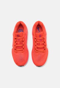 Helle orange Sport Schuhe mit einemMesh-Obermaterial, strukturierten Details, gepolsterter Zunge und einem weißen Nike-Swoosh-Akzent an der Seite.