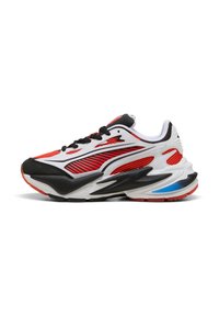 Zapatilla deportiva de corte bajo en rojo, blanco, negro y azul con paneles de malla, parte frontal con cordones y suela acolchada, vista lateral.