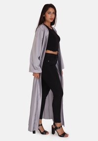 Raso argento lungo sopra un top crop nero e jeans skinny neri. Presenta maniche lunghe e apertura frontale. Sandali neri con tacco.