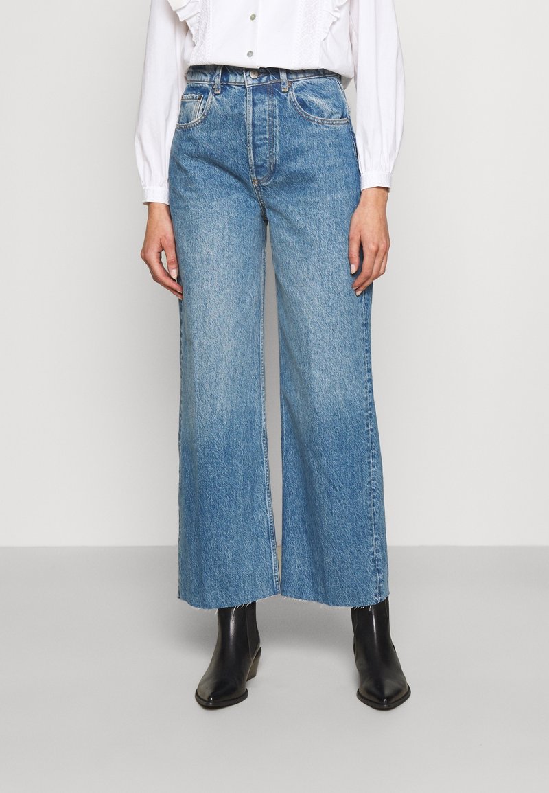Light blue wide-leg jeans made of denim feature a raw hem, high waist, and classic five-pocket design, paired with black ankle boots.