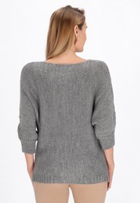 Grauer gestrickter Pullover mit lässiger Passform, weitem Ausschnitt und gerippten Bündchen. Das strukturierte Material weist ein dezentes Muster auf.