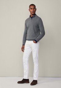 Šedá pletená mikina se zipem, nošená přes námořnickou košili. V kombinaci s bílými slim fit kalhotami a tmavě hnědými semišovými botami.