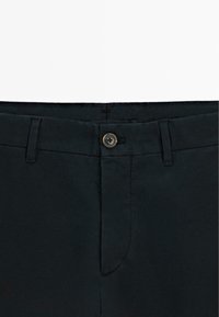 Schwarze Baumwollmischungshose mit flacher Vorderseite, Gürtelschlaufen und einem einzigen Knopfverschluss. Glatte Textur mit unauffälligen Seitentaschen.