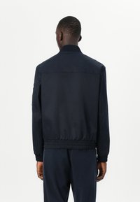 Veste de bombardier navy avec col côtelé et ourlet élastiqué. Tissu lisse avec poches latérales et fermeture éclair à l'avant.