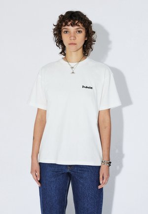 Witte T-shirt met korte mouwen en een klein zwart "Ddenim"-logo op de linkerborst, gedragen met blauwe spijkerbroeken, met een ontspannen pasvorm en een onopgesmukte uitstraling.