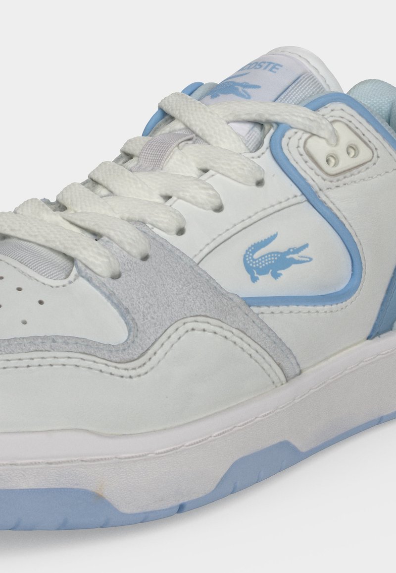 Weißer und hellblauer Sneaker mit weißen Schnürsenkeln, strukturierten grauen Wildlederdetails und einem blauen Lacoste-Krokodil-Logo an der Seite.