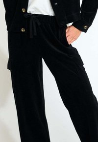 Schwarze Cordhosen mit einem Kordelzugbund, Seitentaschen und einem lockeren Schnitt. Der Stoff hat eine gerippte Struktur und eine weiche, langlebige Oberfläche.