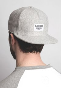 Siva bejzbolska kapa s ravnim vizirjem, ki ima na sprednji strani belo etiketo z oznako "BLACKSKIES". Ponuja preprost dizajn.