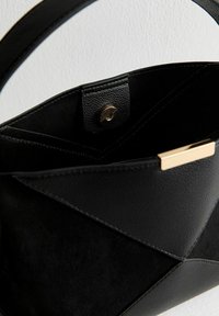 Bolso negro con una combinación de texturas lisas y de ante. Presenta una placa de acento dorada y un cierre de presión seguro en el interior.