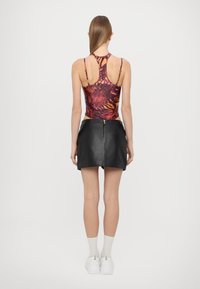 Raštuotas bodysuit su oranžiniu ir violetiniu dizainu, derinamas su juoda dirbtinės odos mini sijonu, išryškinančiu užtrauktuko detalę nugaros pusėje.