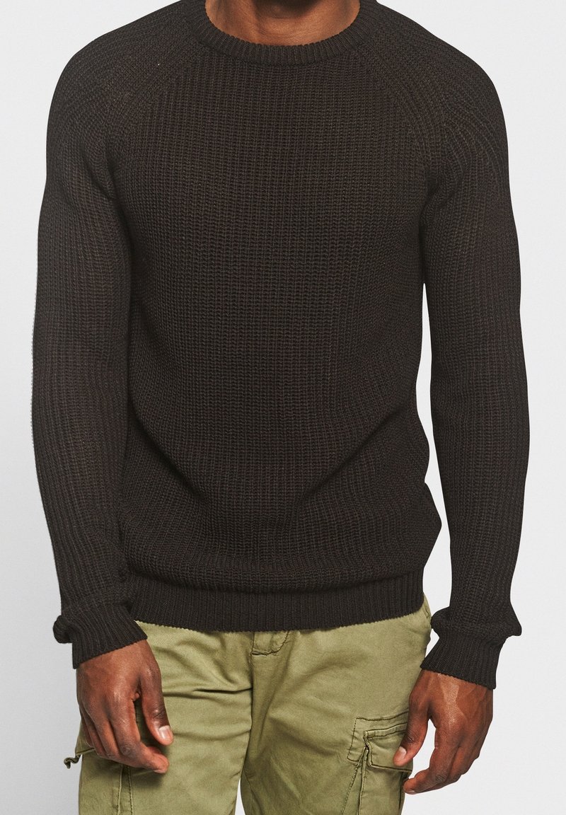 Pull en maille noir avec un col rond et des poignets côtelés. Présente un motif texturé et une coupe régulière. Associé à un pantalon cargo vert clair.